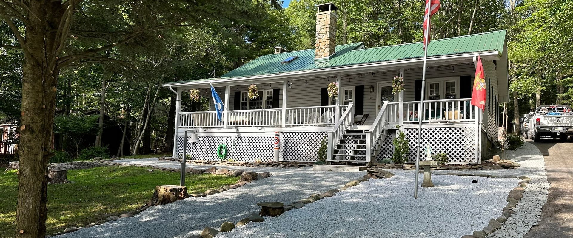 White cottage with green roof and a gravel walkway lined with white stones. Trees in background.