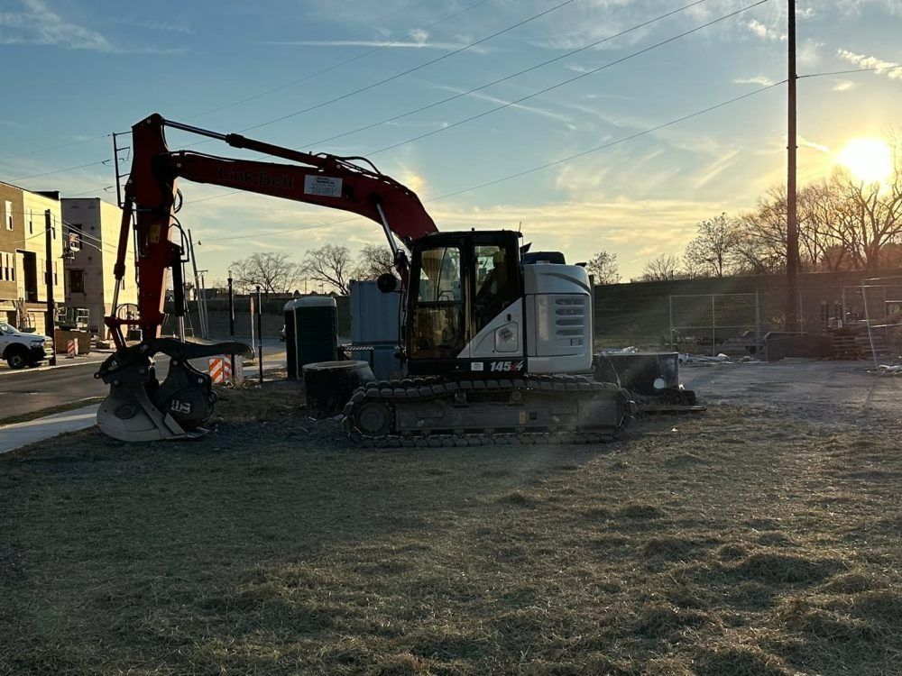 An excavator on a construction site with the sun setting in the background.