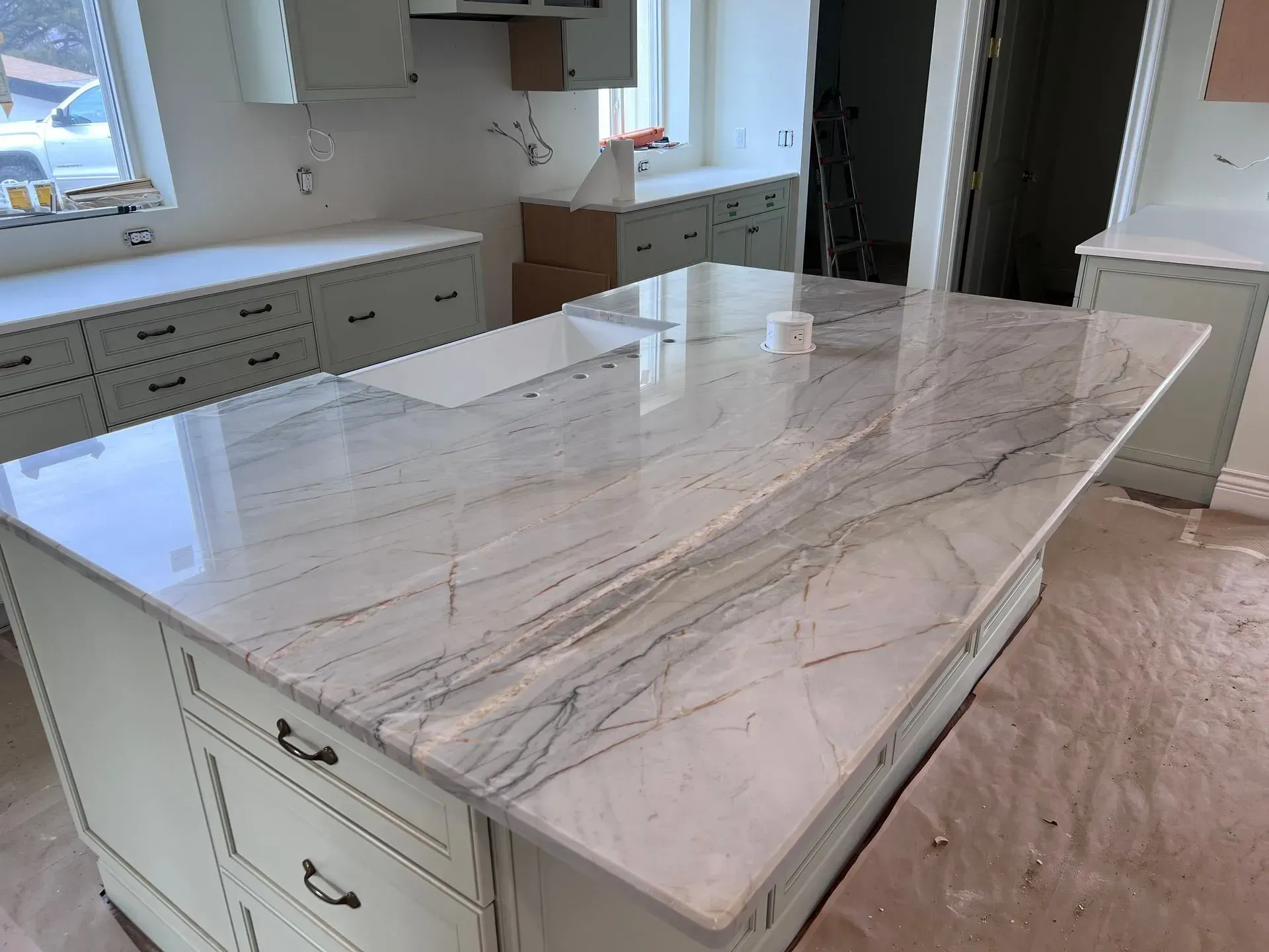 A kitchen with white cabinets and a large marble counter top.