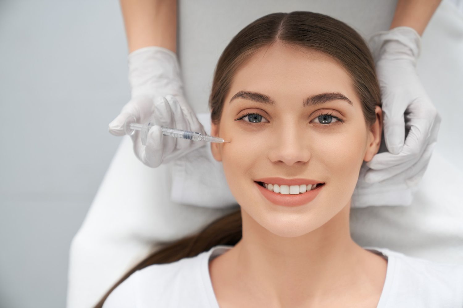 A woman is smiling while getting a botox injection in her face.