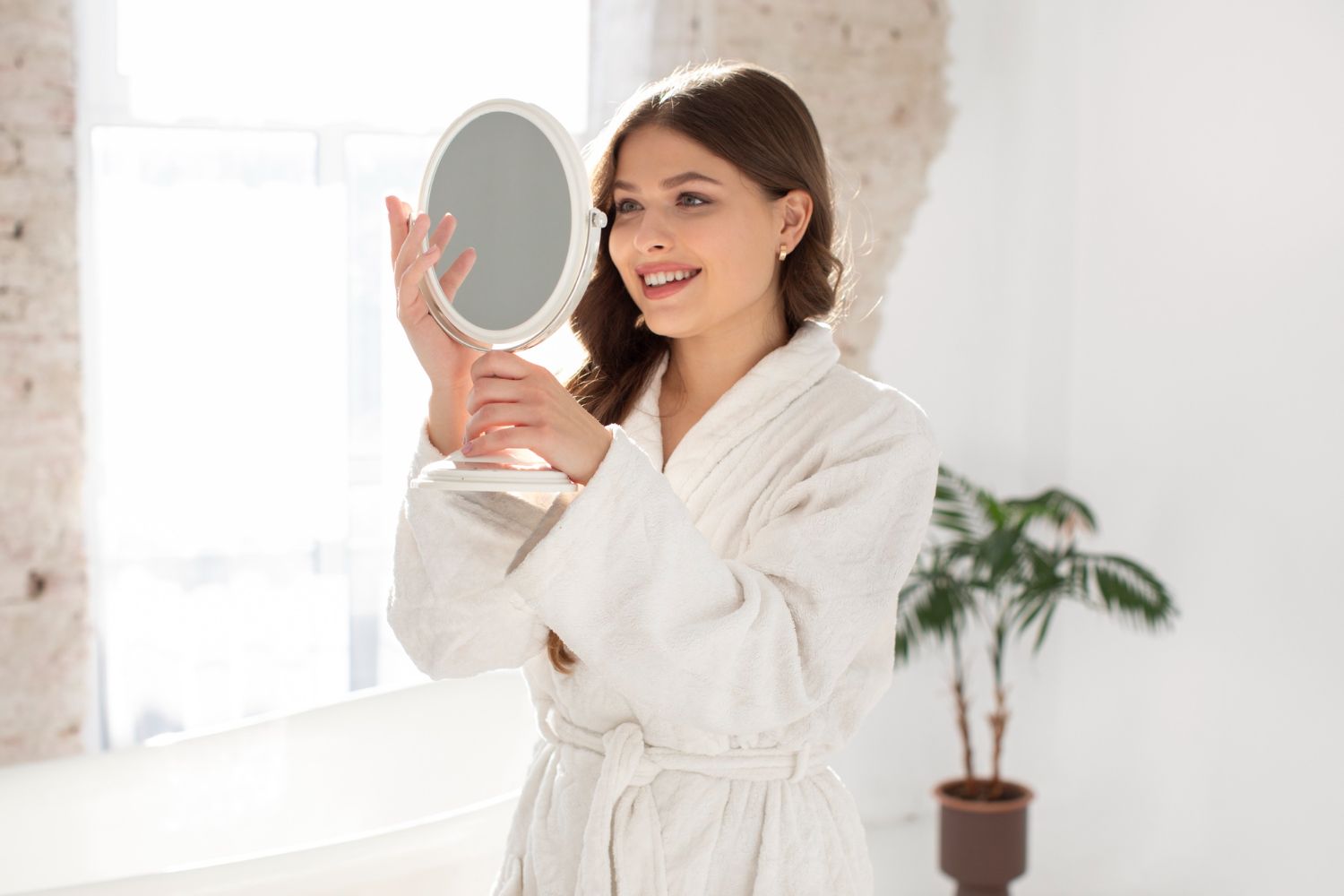 A woman in a bathrobe is looking at herself in a mirror.