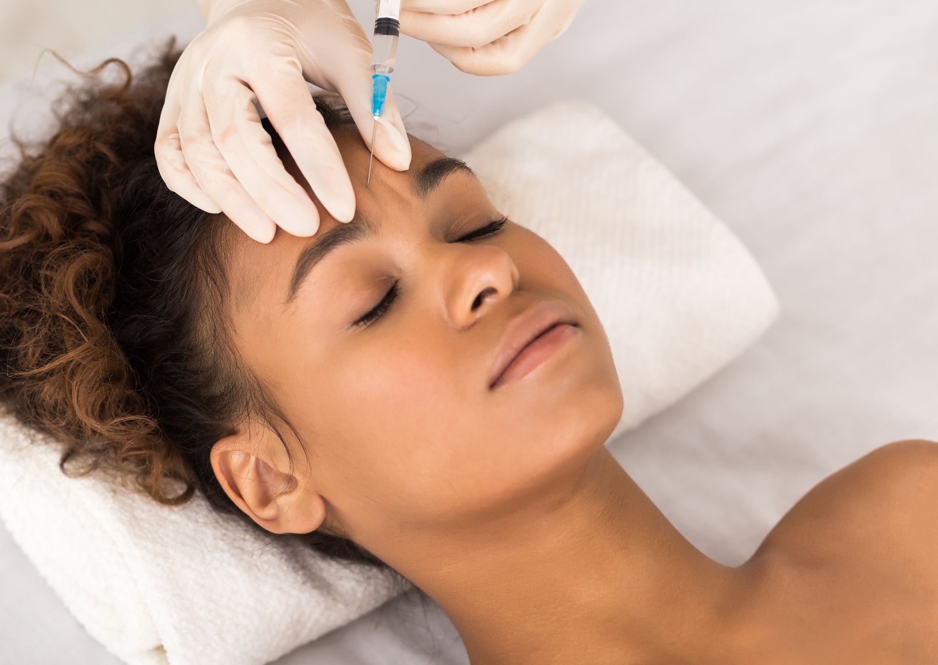 A person receiving an injection in the forehead while lying down on a white towel.