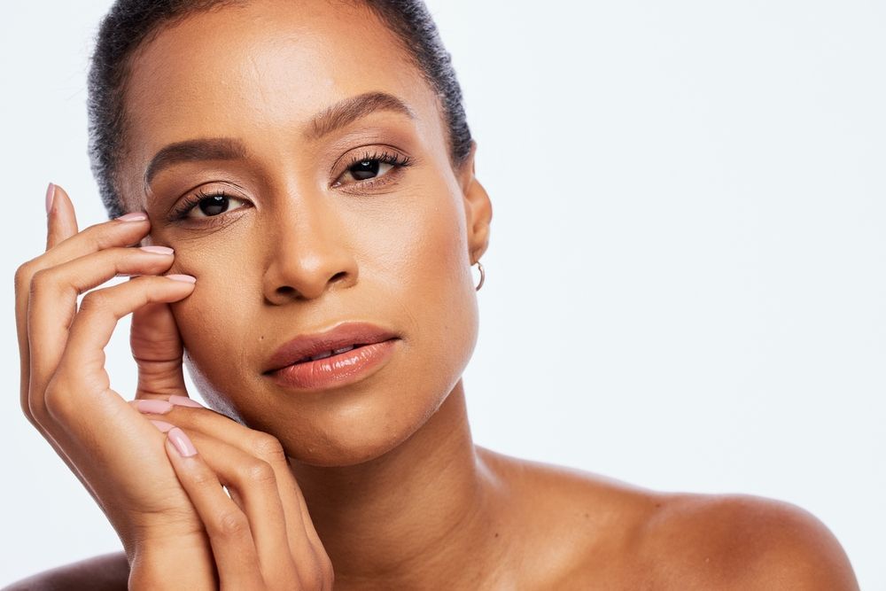 A woman is touching her face with her hand and looking at the camera.