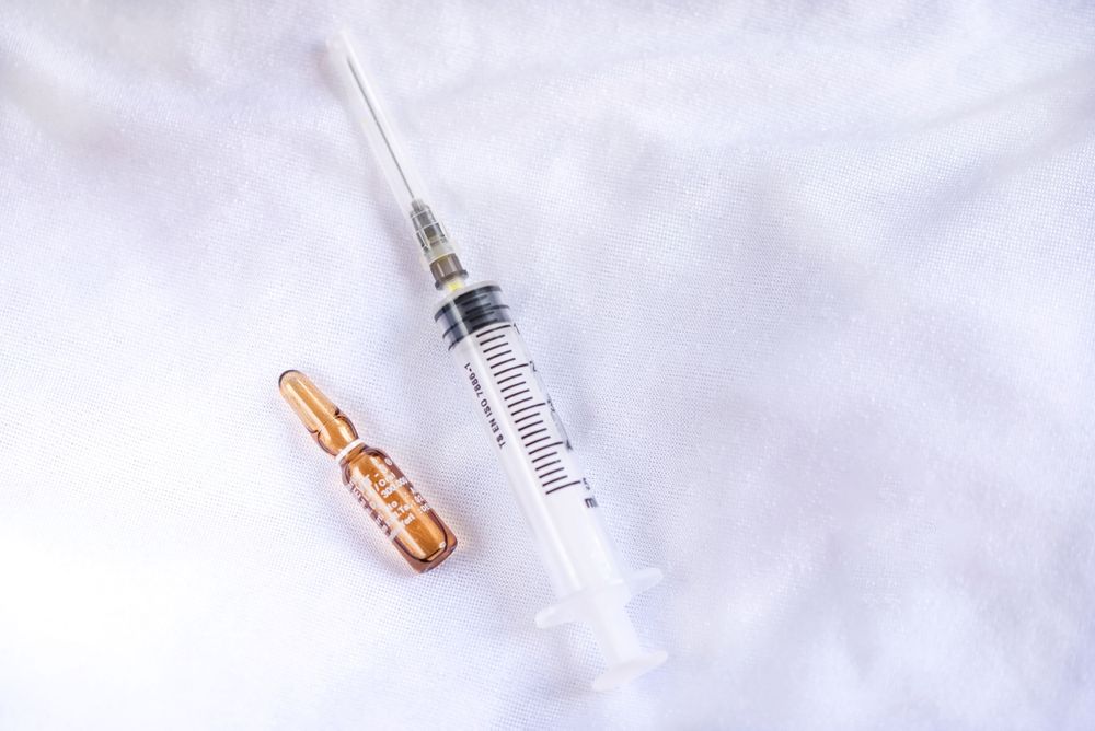A syringe and an ampoule are on a white surface.