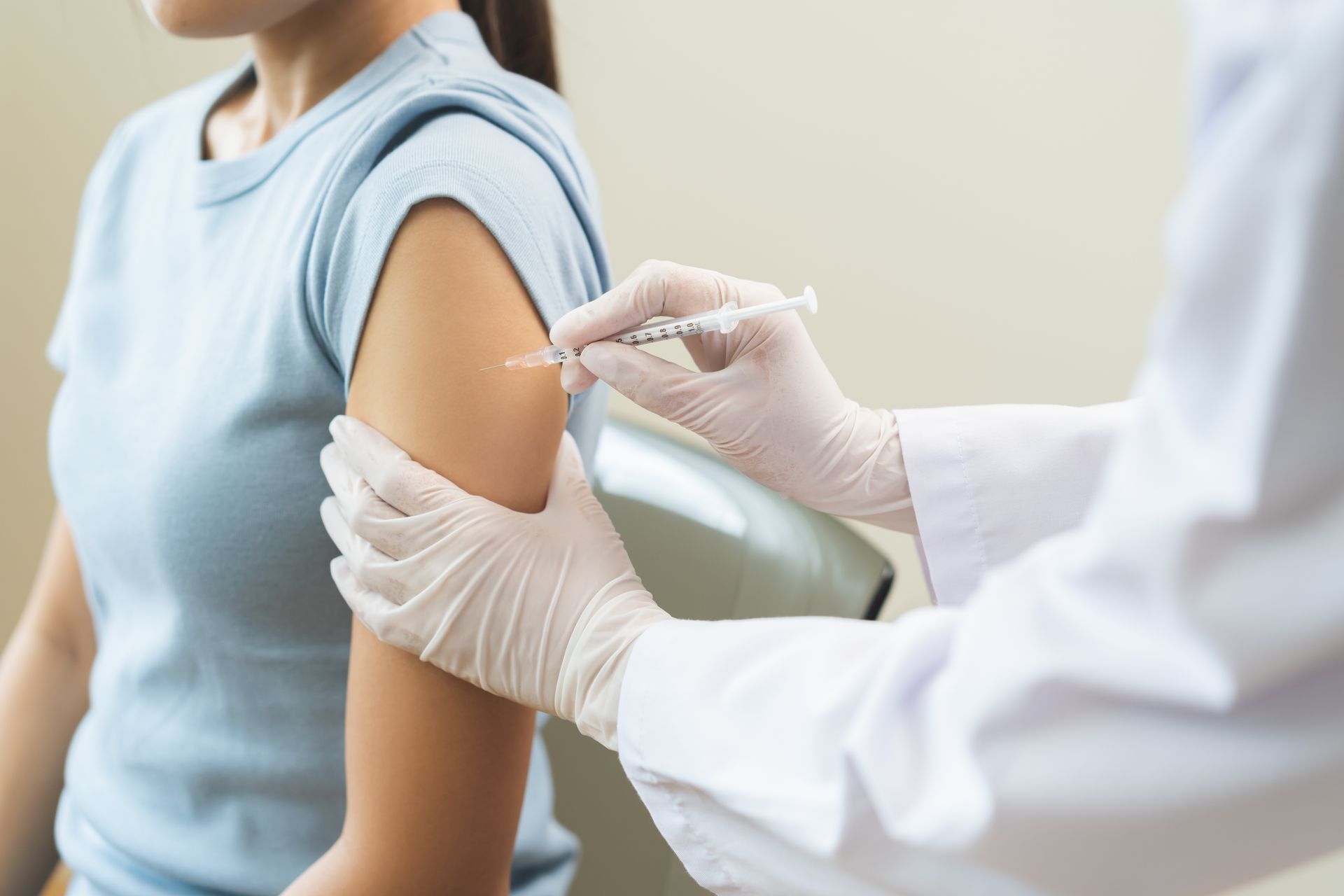 Person receiving an injection in their upper arm by a gloved hand.