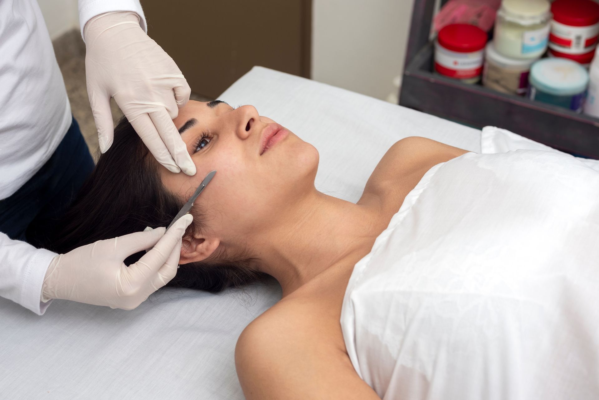 Woman receiving facial treatment, gloved hands hold a tool near her cheek.