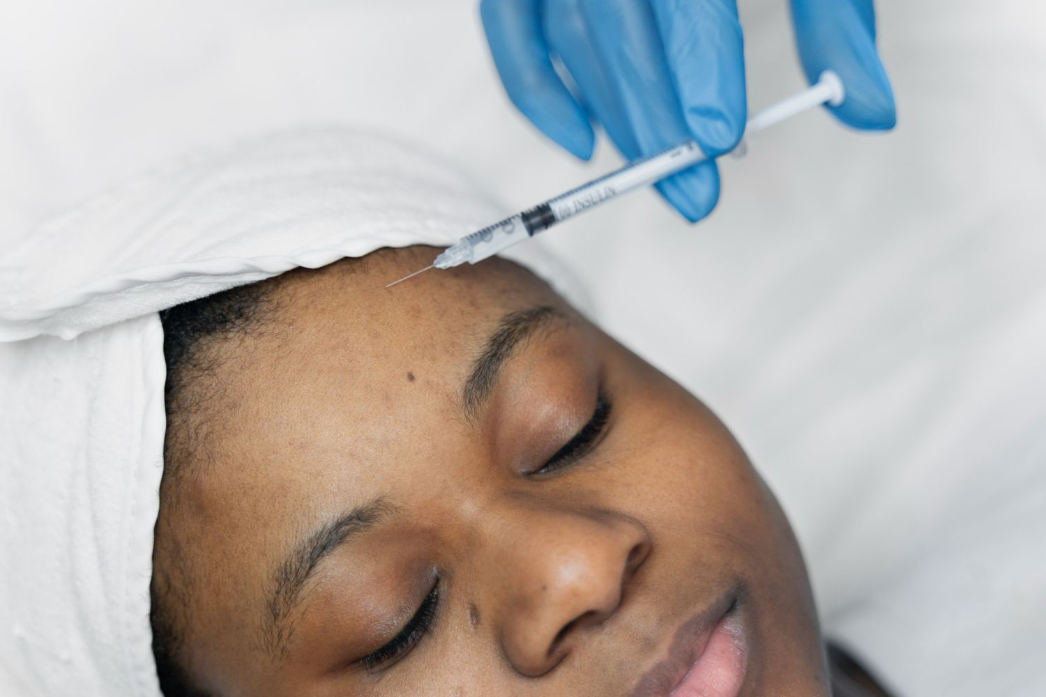 Person receiving Botox injection on forehead, eyes closed, clinic setting.
