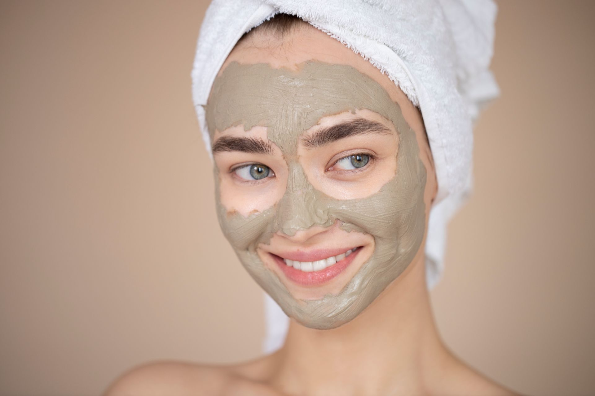 A woman with a towel wrapped around her head is wearing a clay mask on her face.