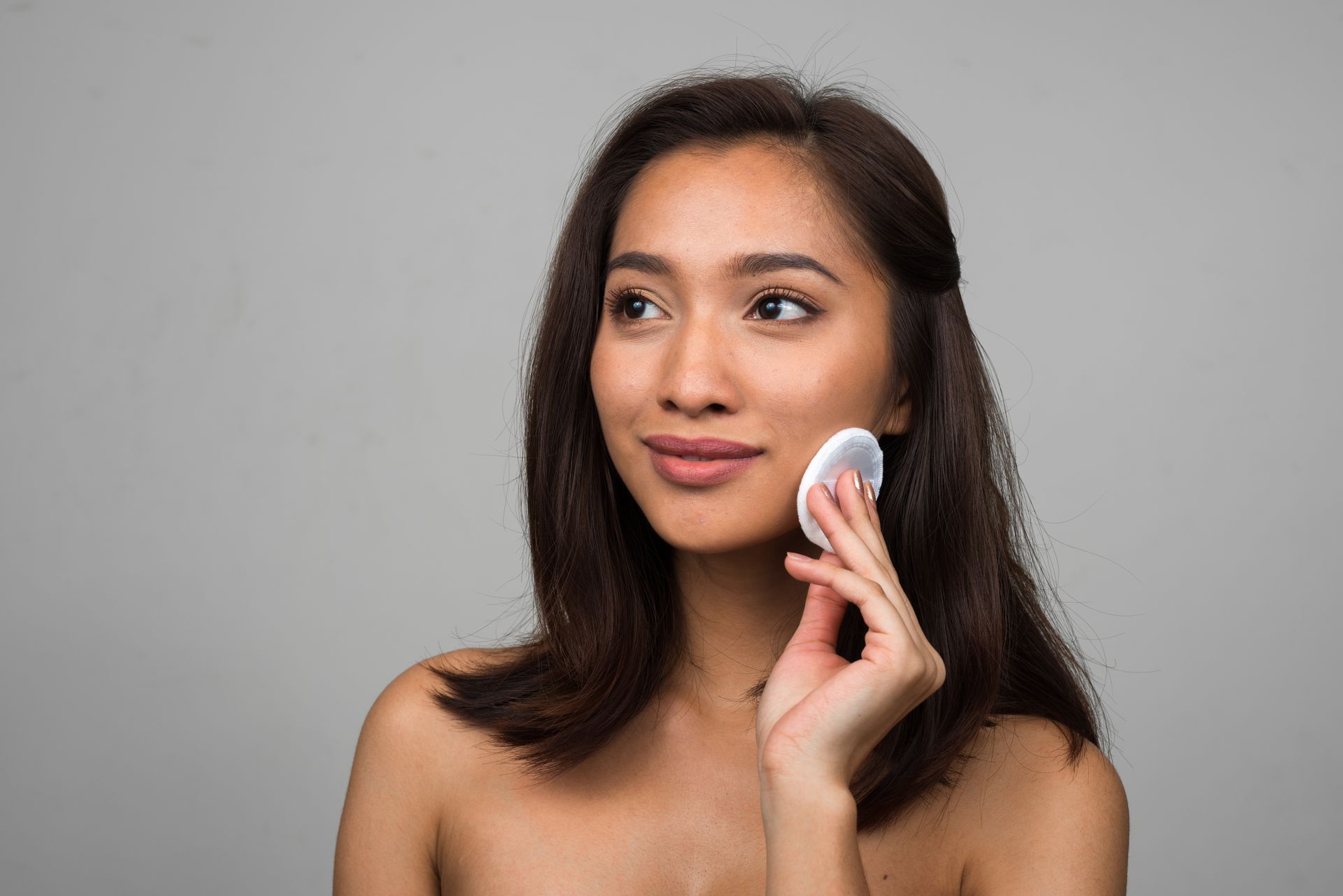 A woman is cleaning her face with a cotton pad.