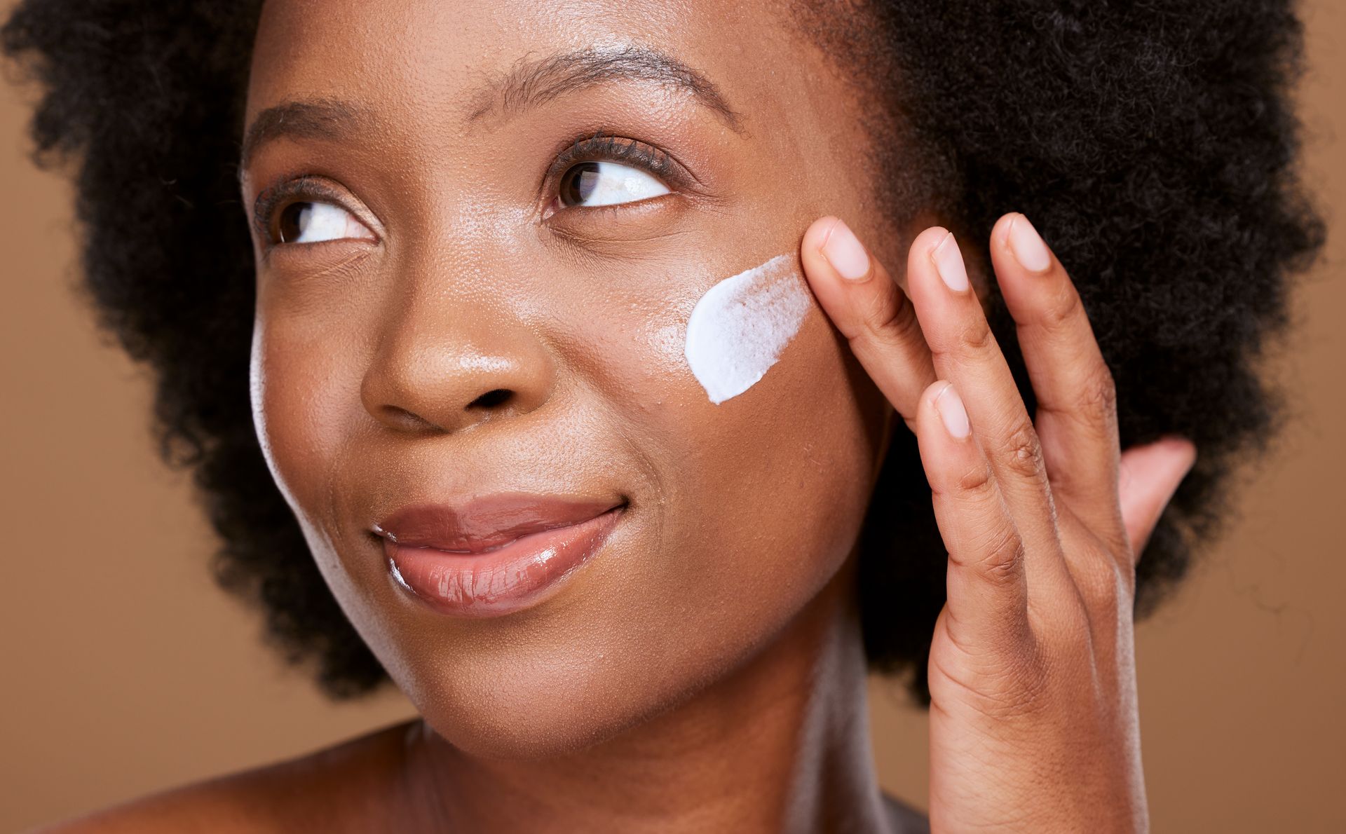 A woman is applying lotion to her face.