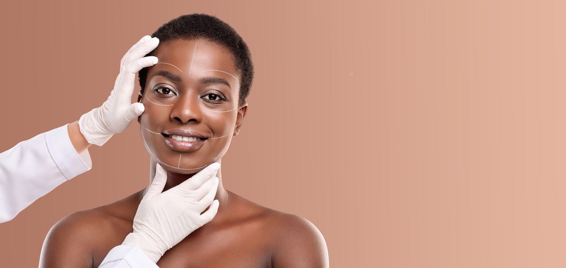 Portrait of a smiling person with gloved hands gently touching the face against a peach background