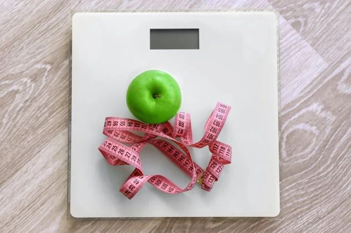 A green apple is sitting on top of a scale next to a measuring tape.