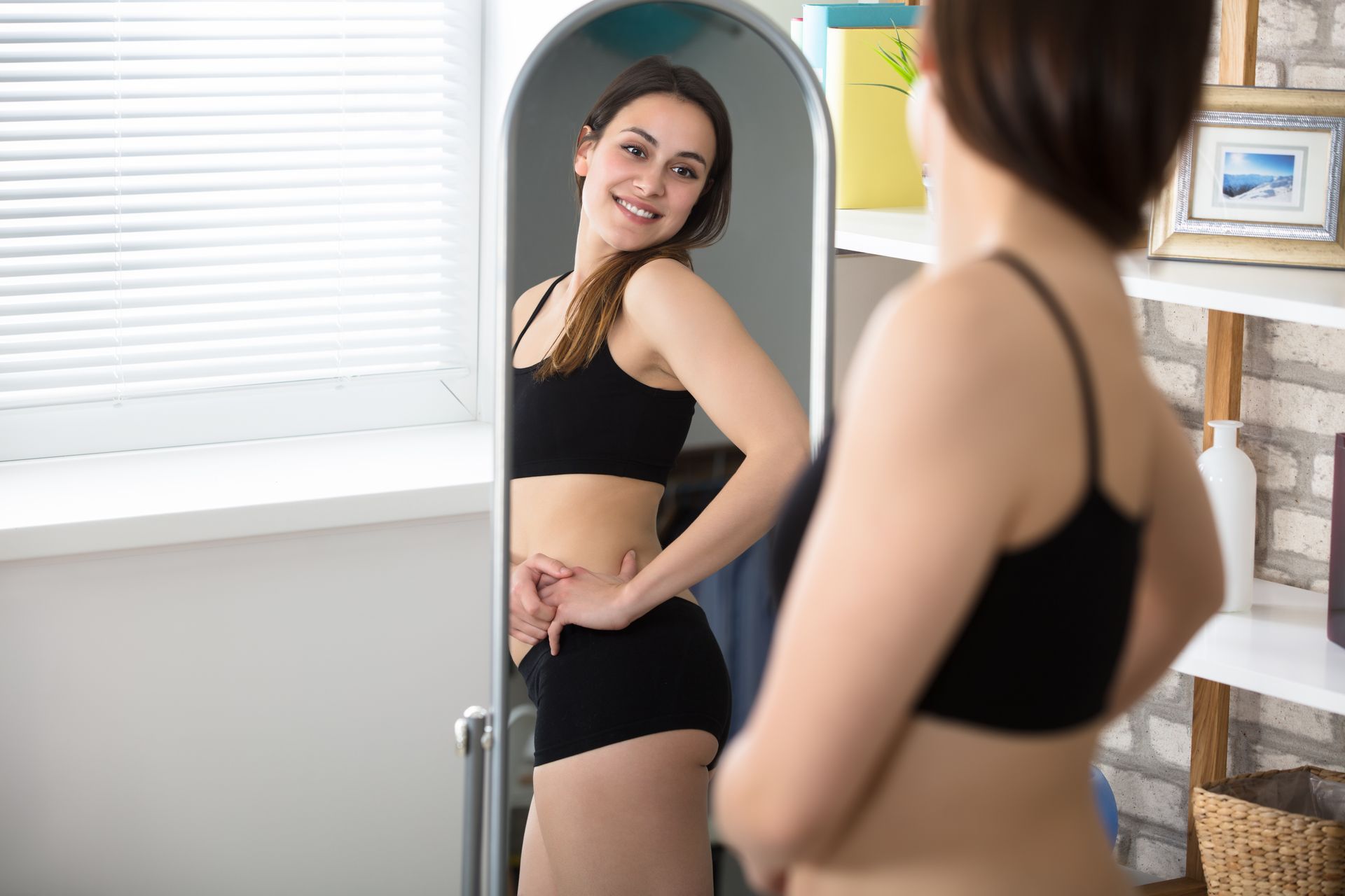 Woman in black workout clothes looking at herself smiling in a mirror.