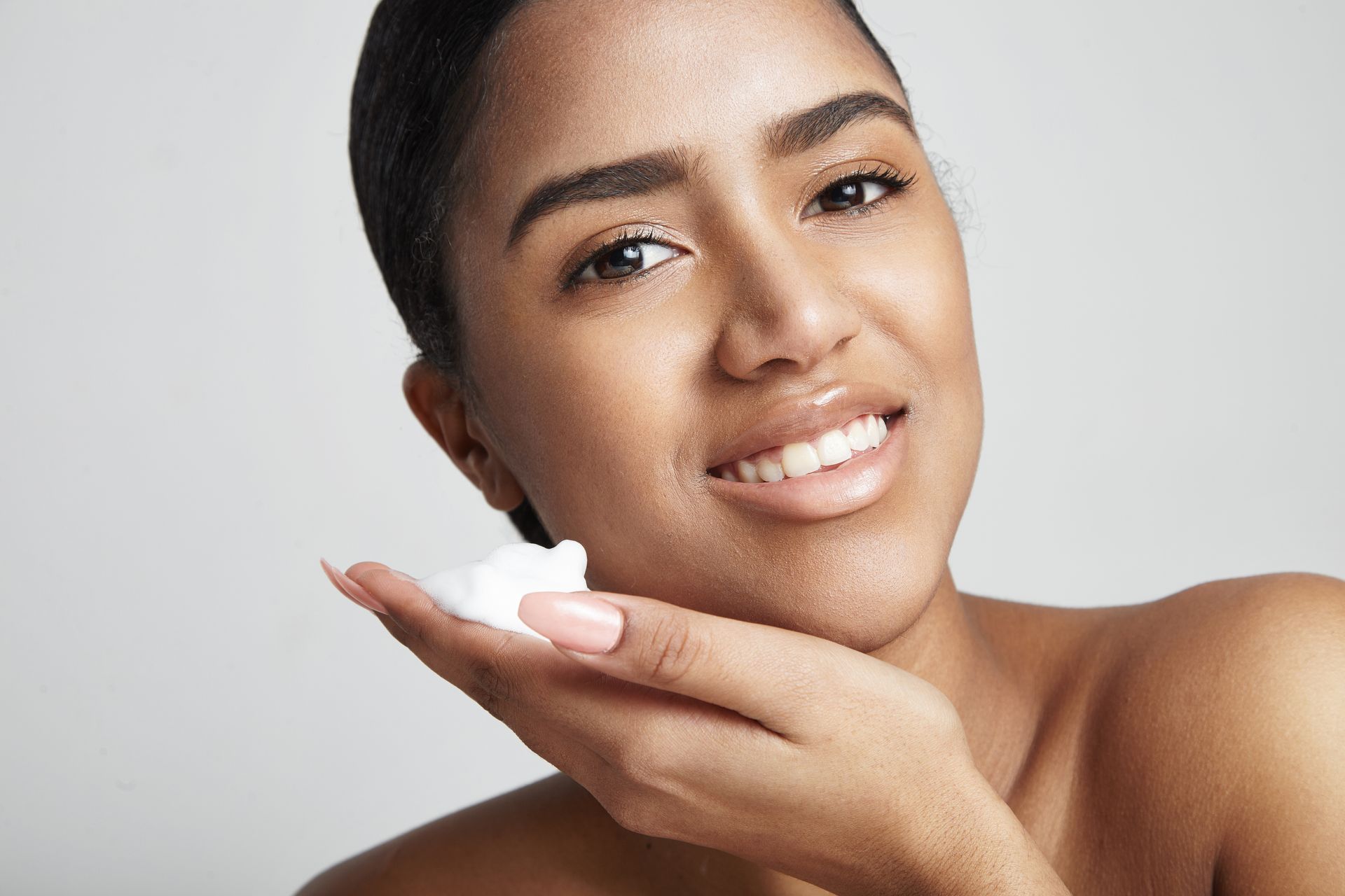 A woman is smiling while holding a sponge to her face.