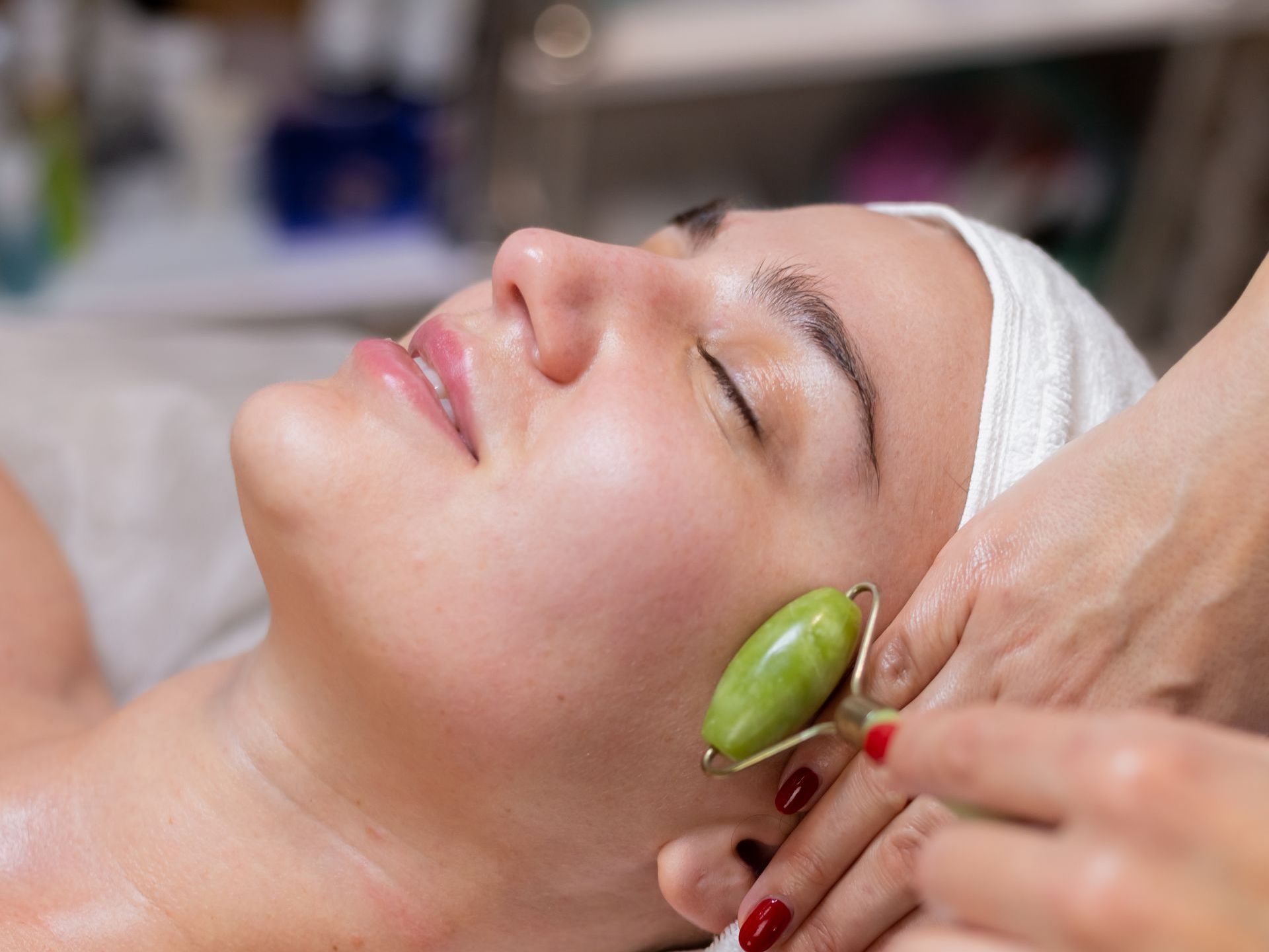 A woman is getting a facial massage with a green jade roller.