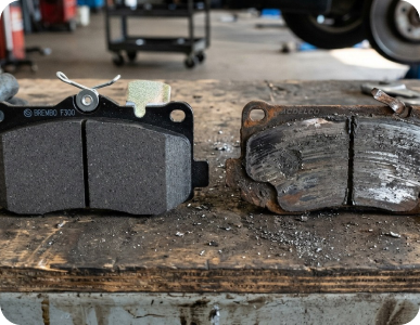 Old and new brake pads side by side on a worn workbench, showing wear and replacement.