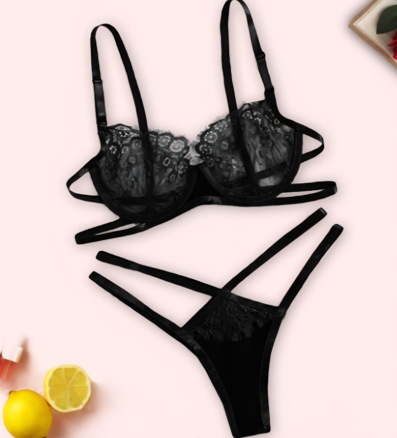 Conjunto de lencería de encaje negro, incluye sujetador con tirantes y tanga a juego, sobre superficie rosa.