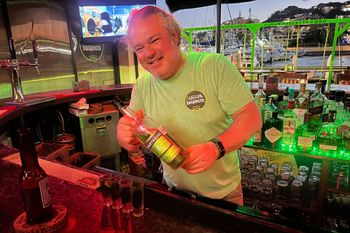 A man is standing behind a bar holding a bottle of liquor.