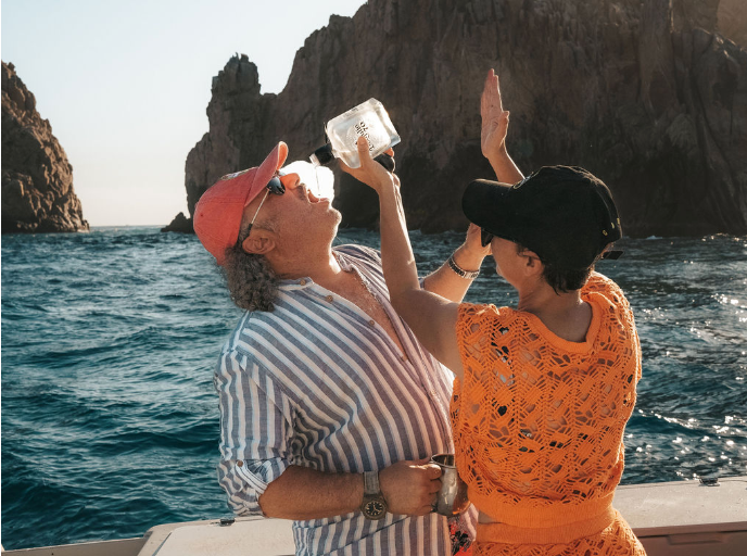 A man is drinking from a bottle while a woman holds up a glass