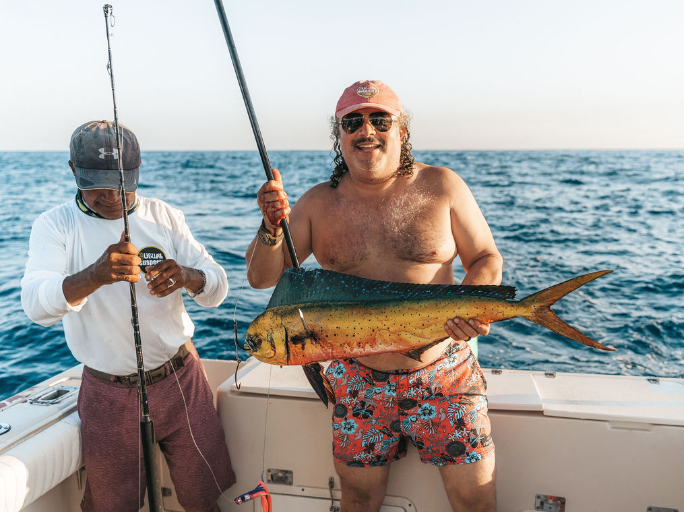 Two men are fishing in the ocean and one of them is holding a large fish.