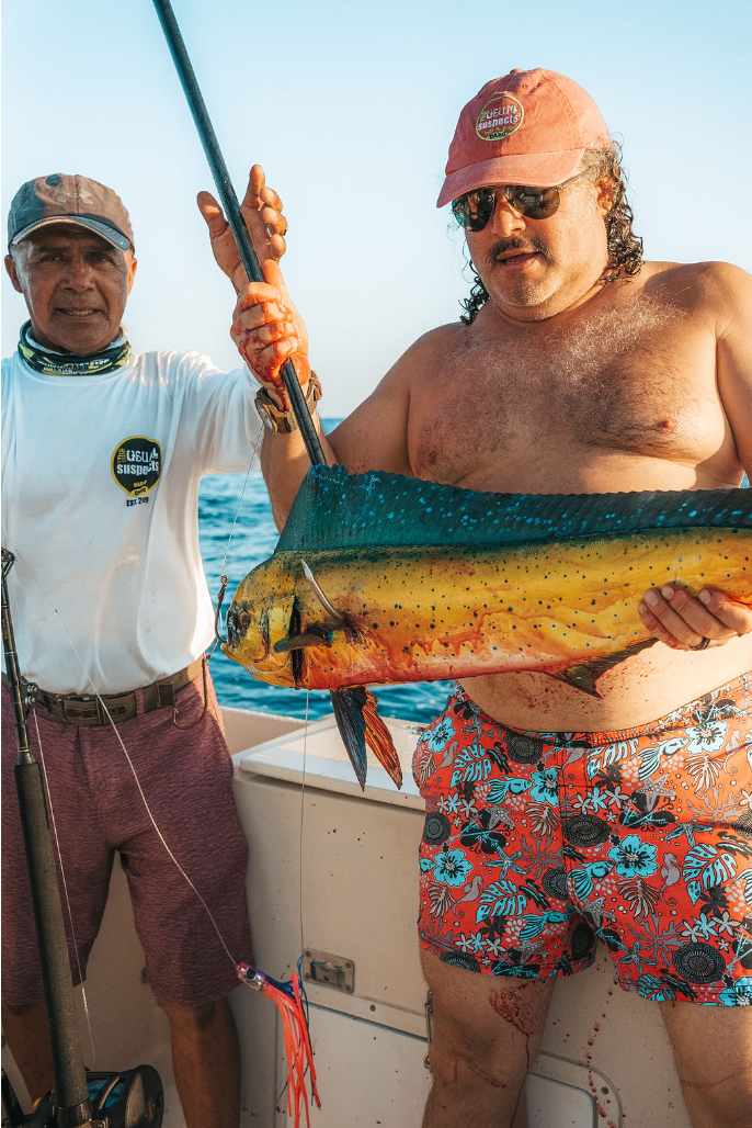 Two men are standing on a boat holding a large fish.