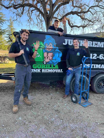 Three people posing beside a junk removal truck, one holding a green recycling bin.