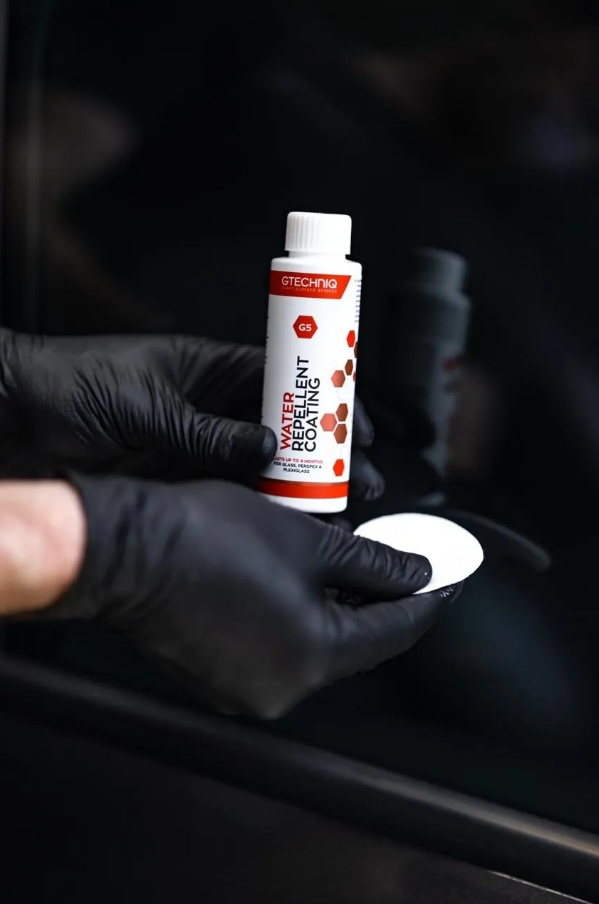 A person wearing black gloves is holding a bottle of product in their hand.