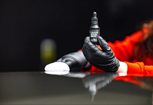 A person wearing black gloves is holding a bottle of polish.