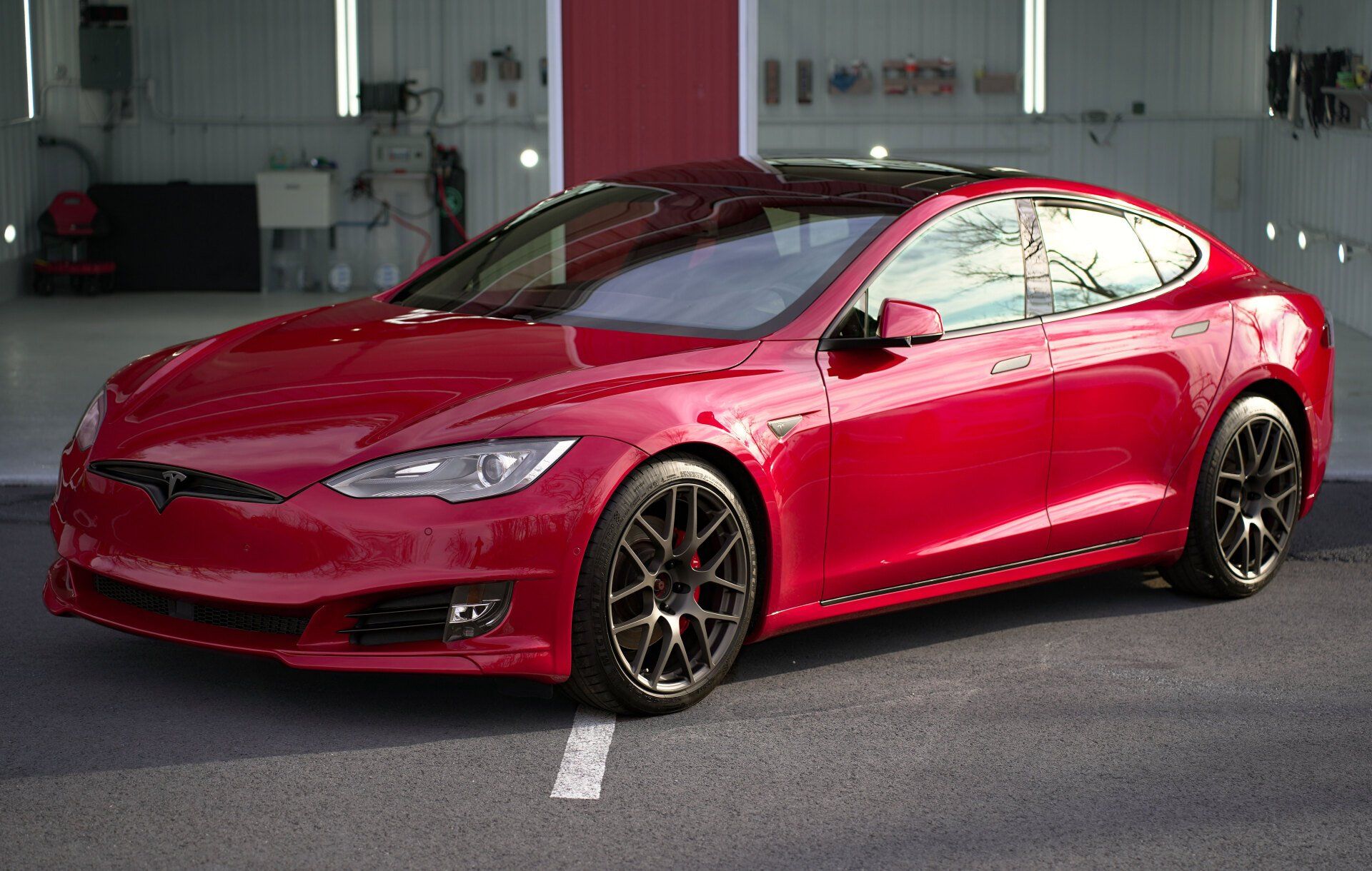 a red tesla model s is parked in a parking lot .