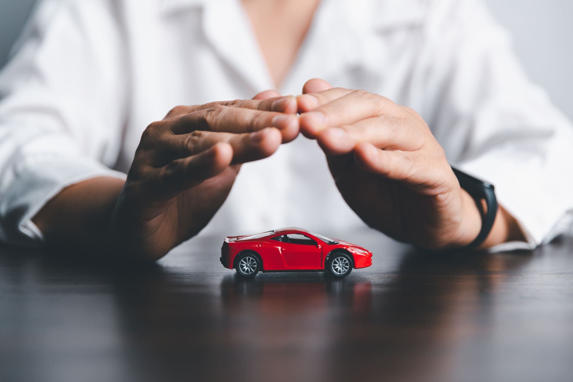 Business woman's hand protecting red toy car on desk. Planning to manage transportation finance costs. Concept of car insurance business, saving buy - sale with tax and loan for new car