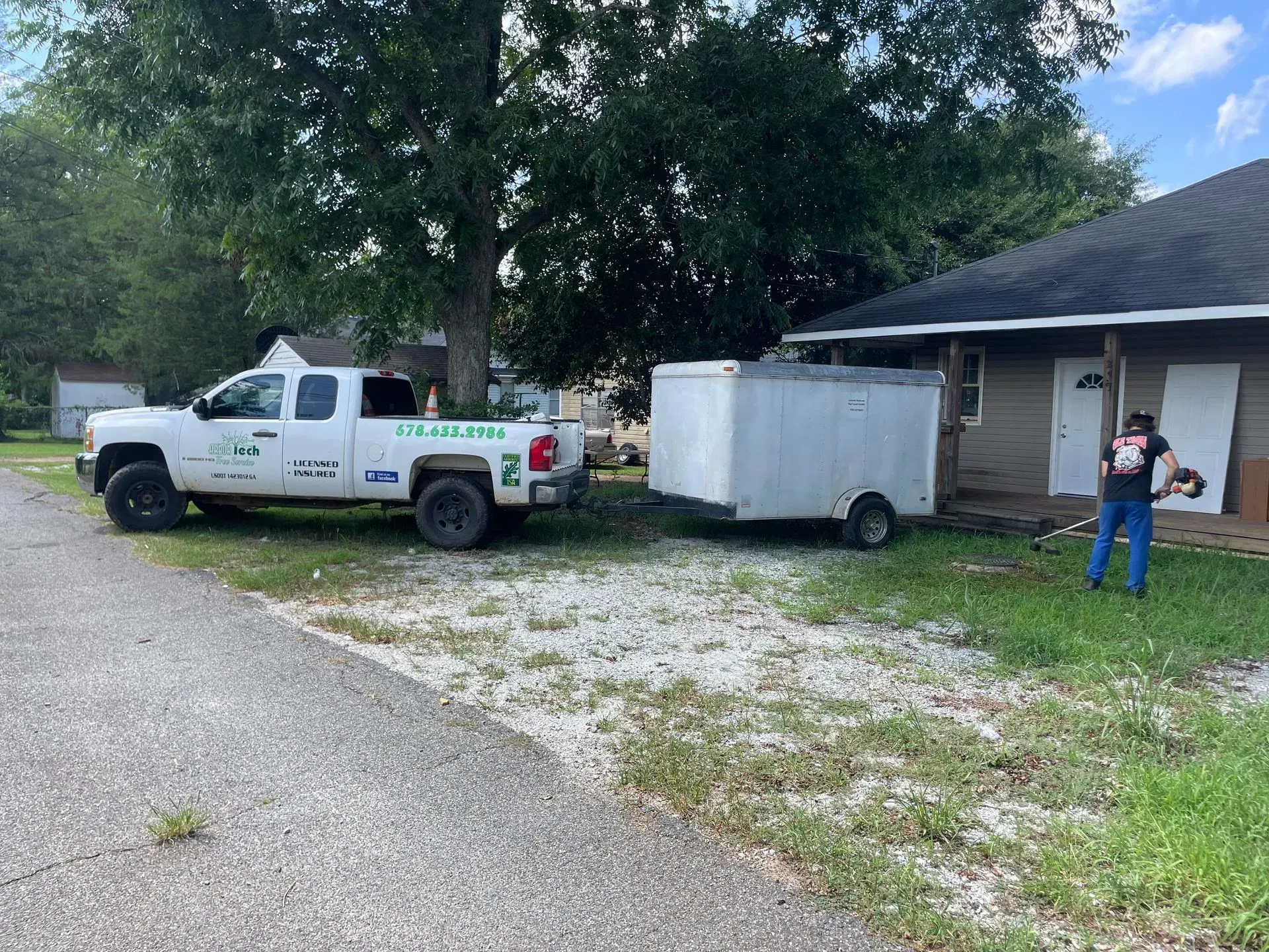 A white truck with a trailer attached to it is parked in front of a house.