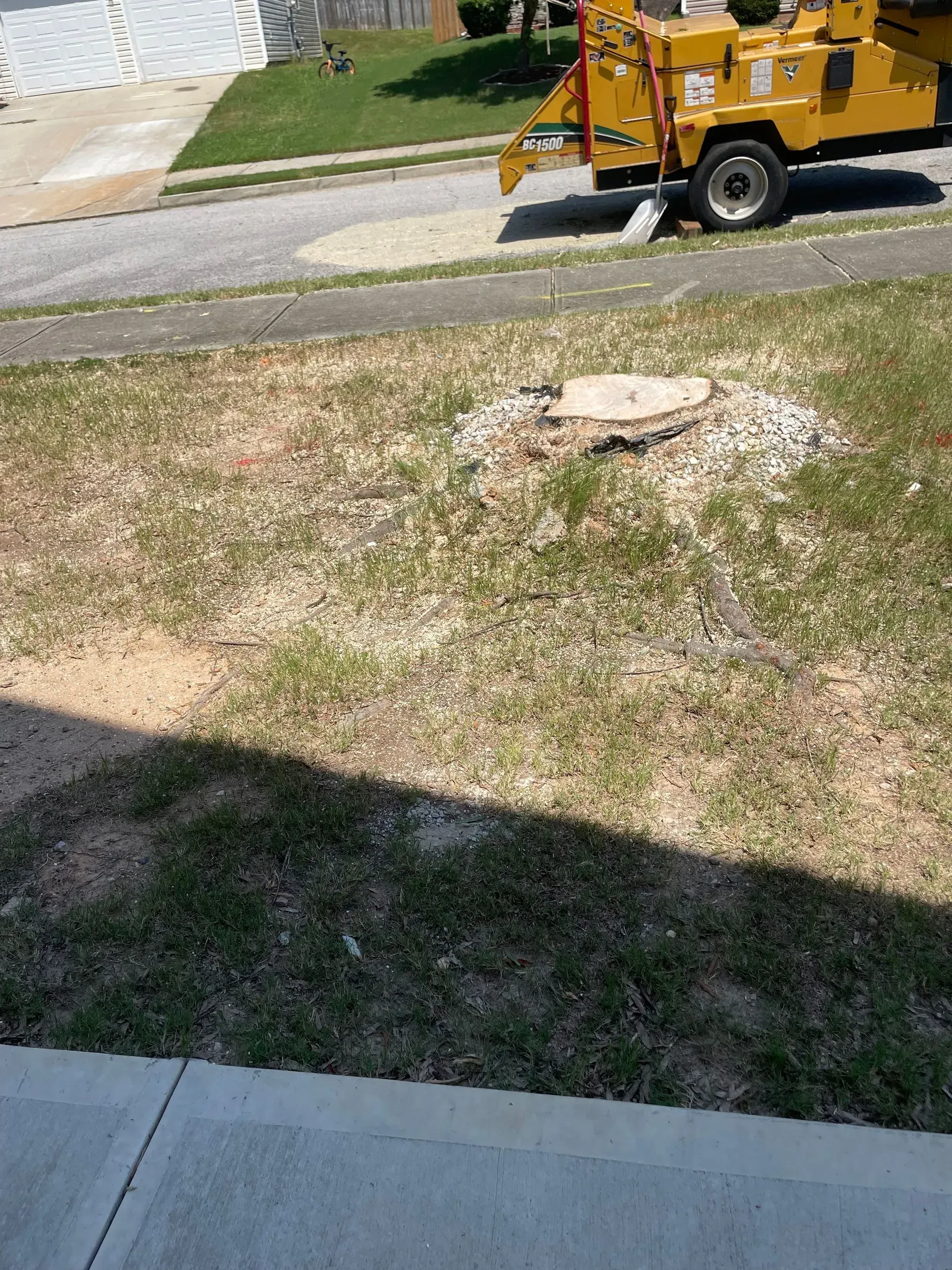 A yellow truck is cutting down a tree stump in a yard.