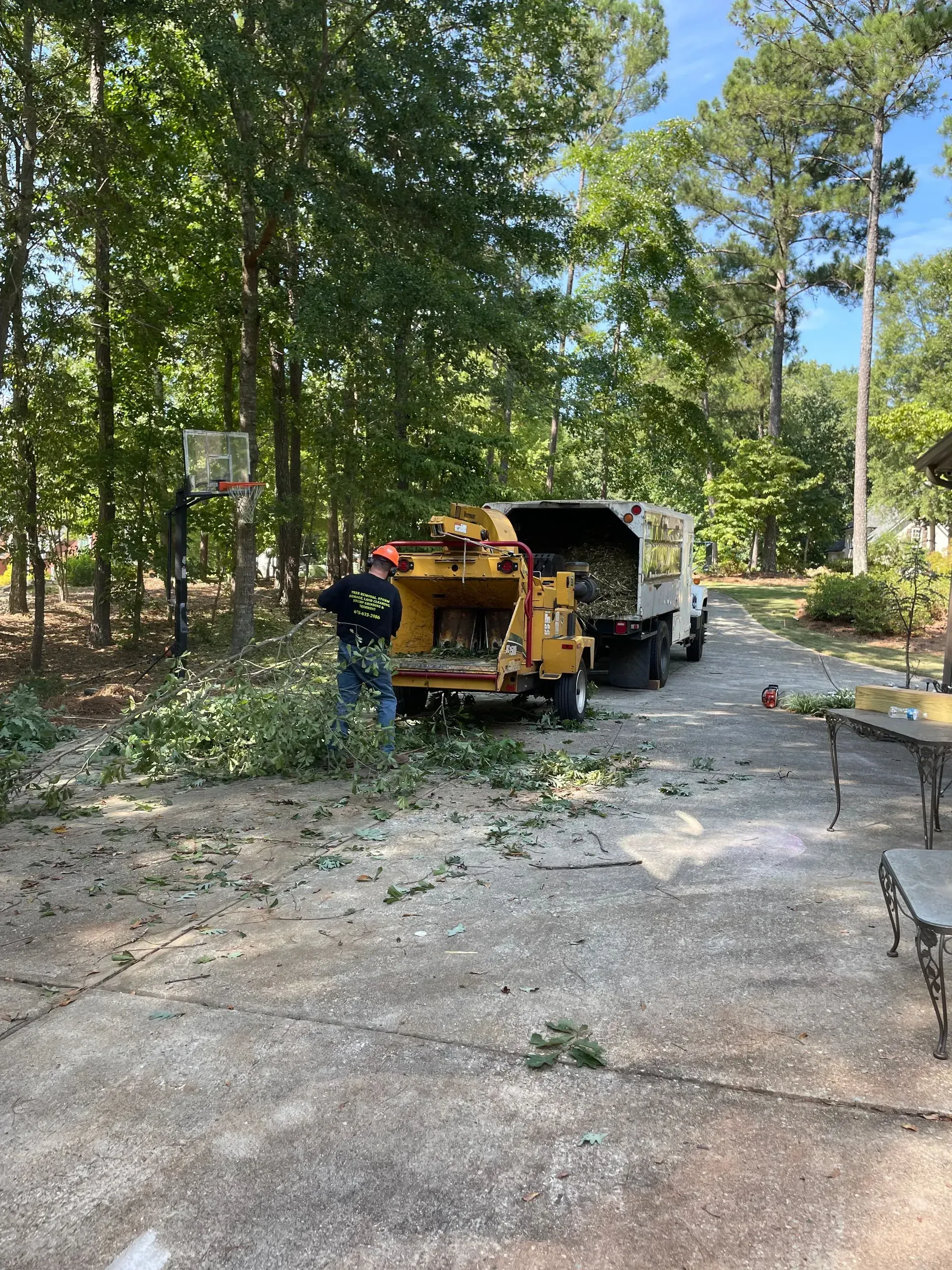 A man is standing next to a tree chipper in a driveway.