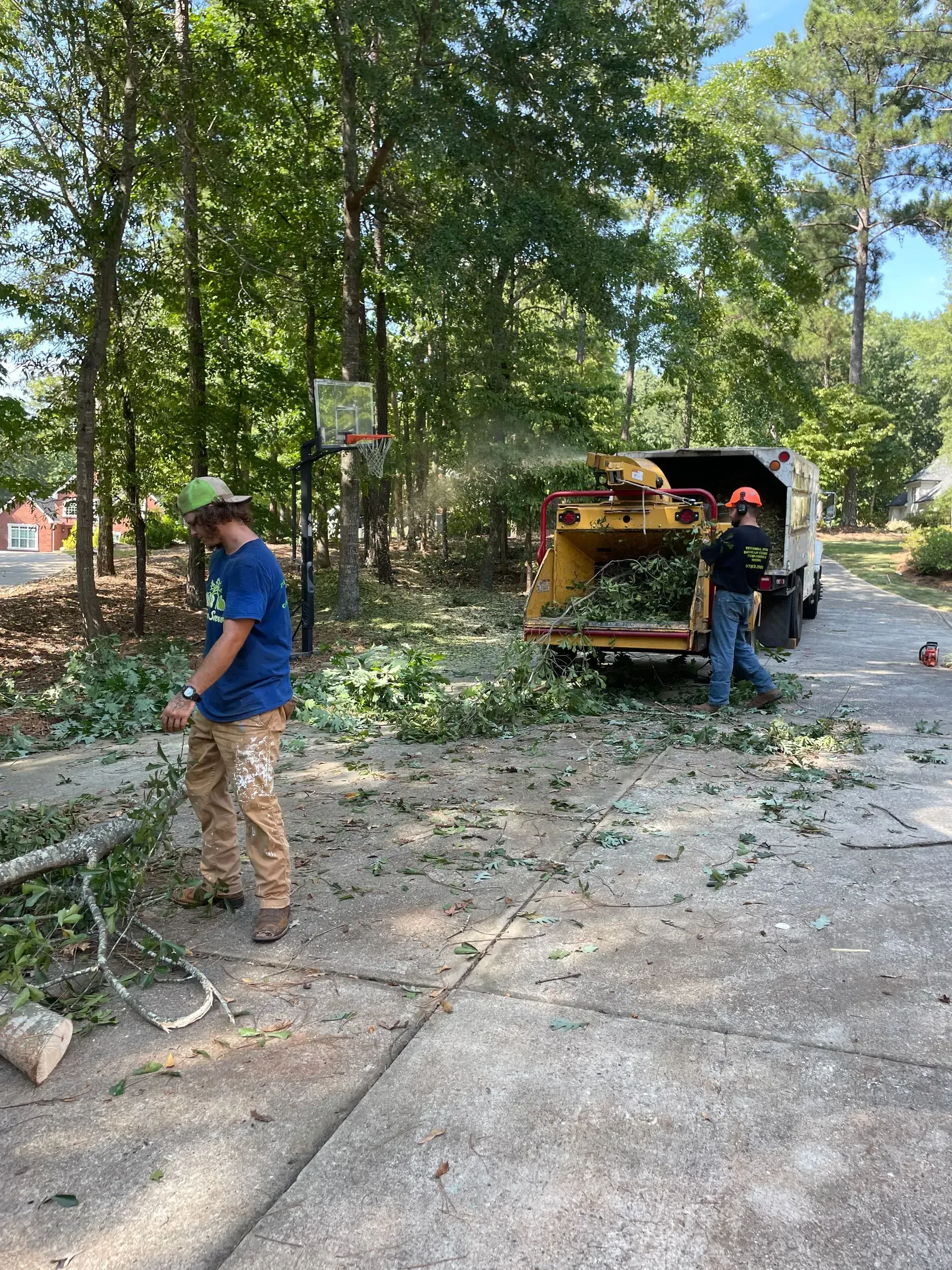 A man is standing next to a tree chipper in a driveway.