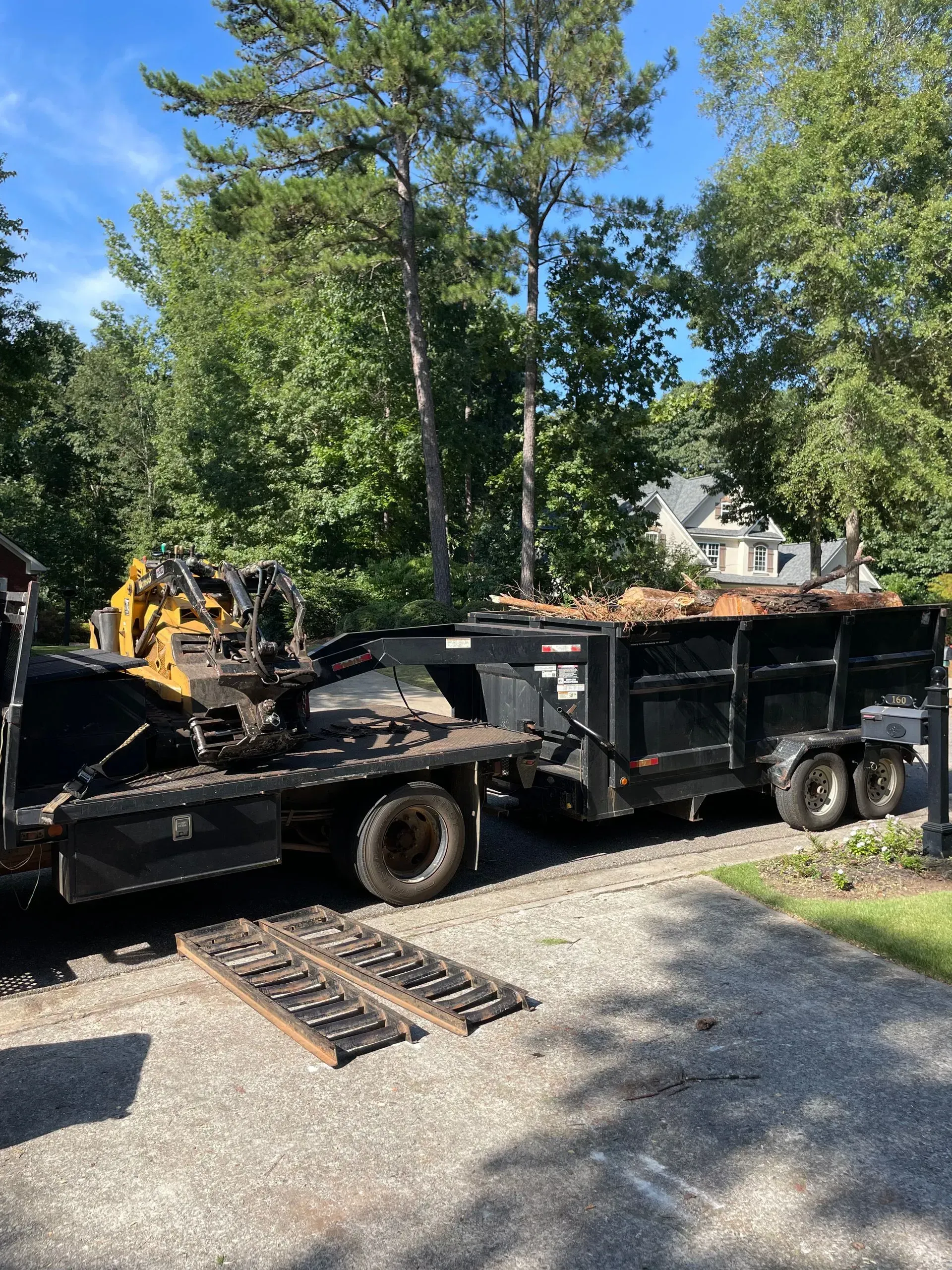 A dump truck with a trailer attached to it is parked in a driveway.