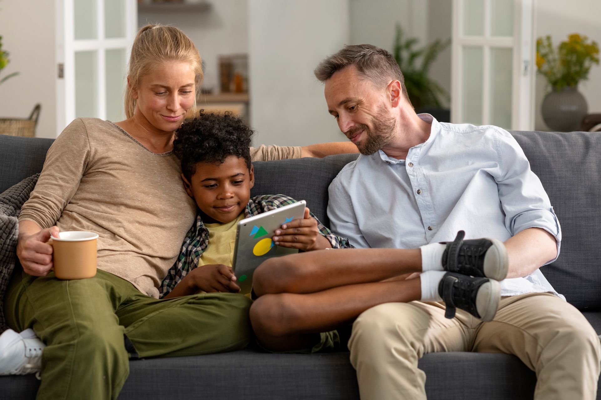 A family is sitting on a couch looking at a tablet.