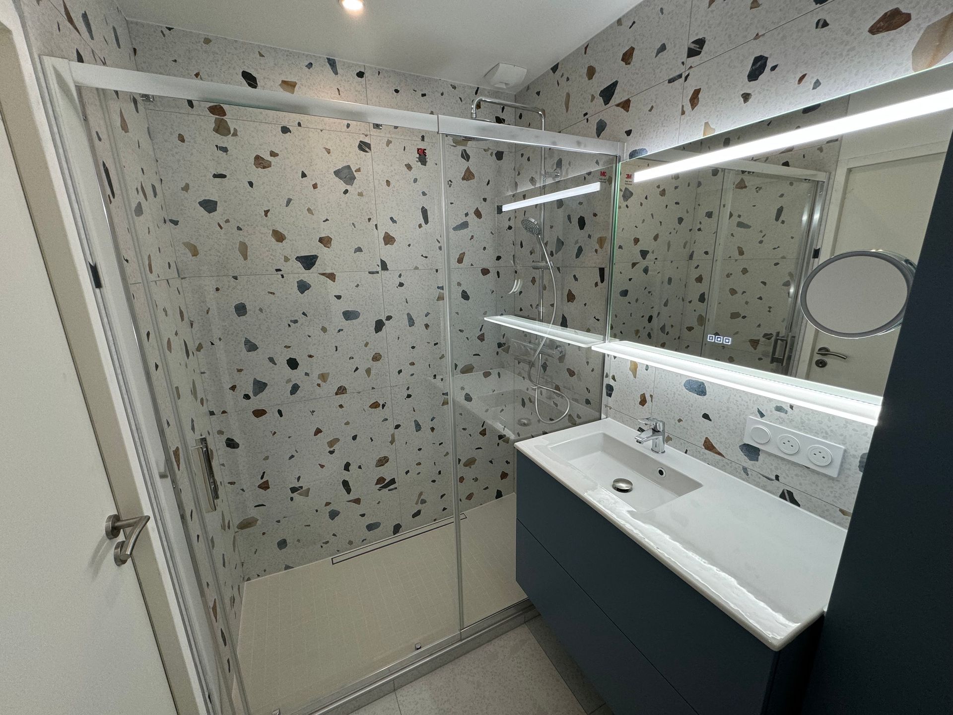 Une salle de bain avec un lavabo, une douche et un miroir.