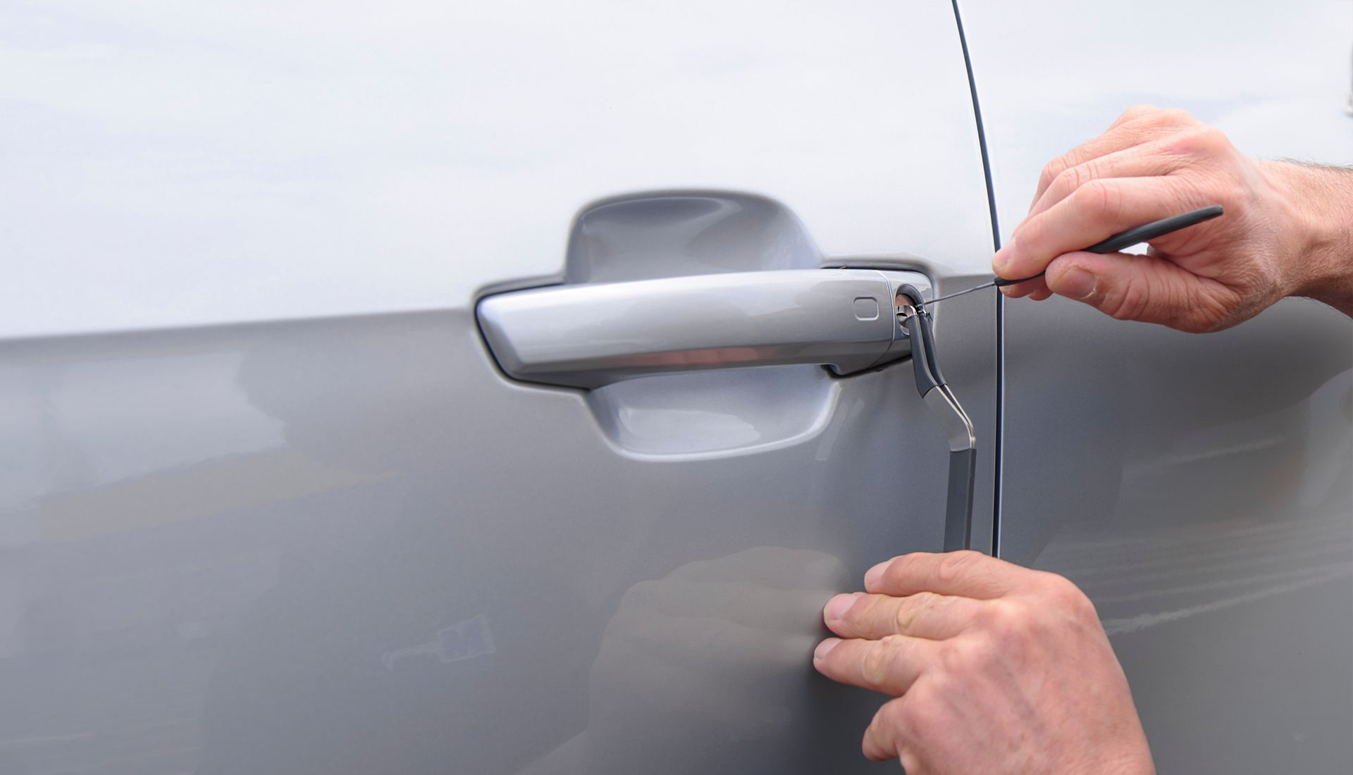 Hands using tools to unlock a car door.