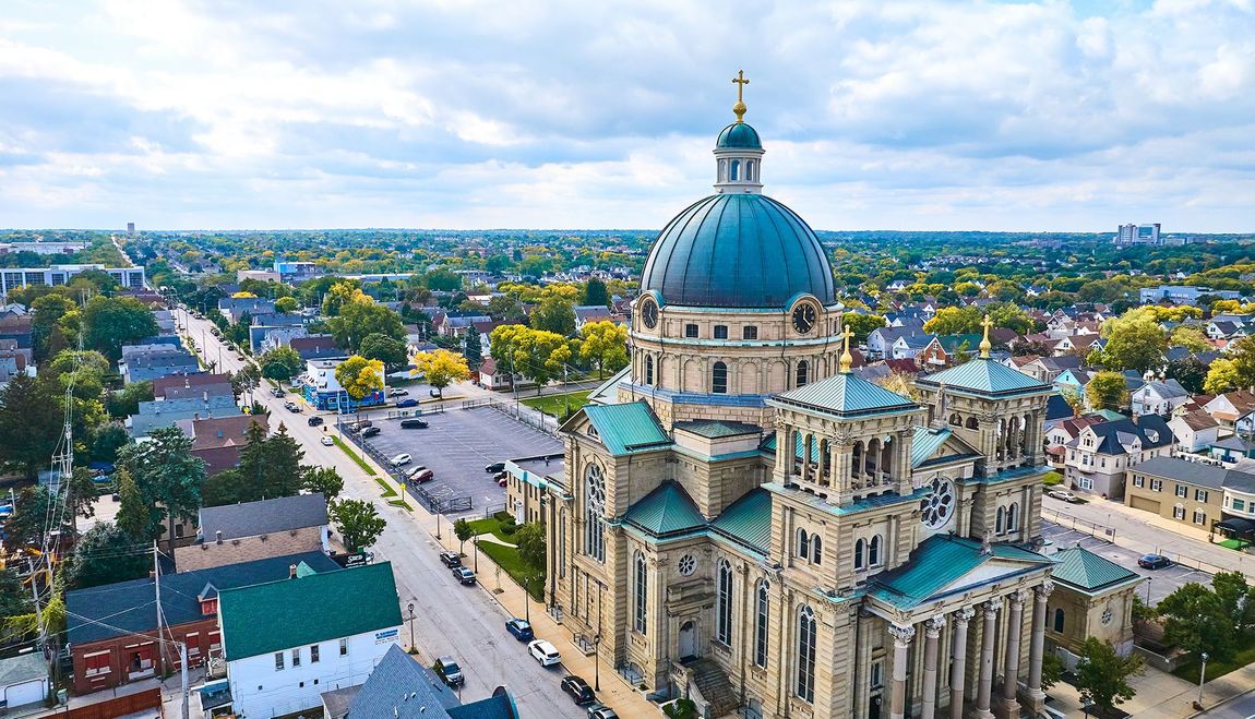 Aerial view of a large church with a blue dome, surrounded by a city and green trees.