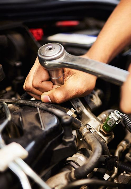 Hands using a wrench to work on a car engine.