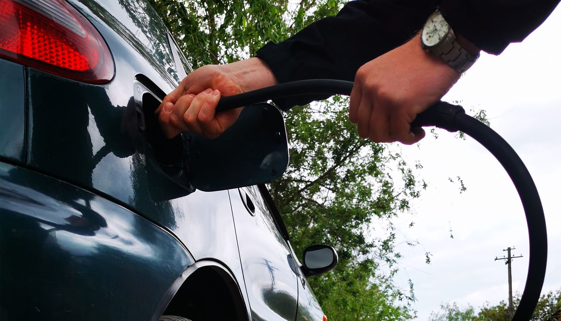 Person fueling a dark green car with a black fuel hose.
