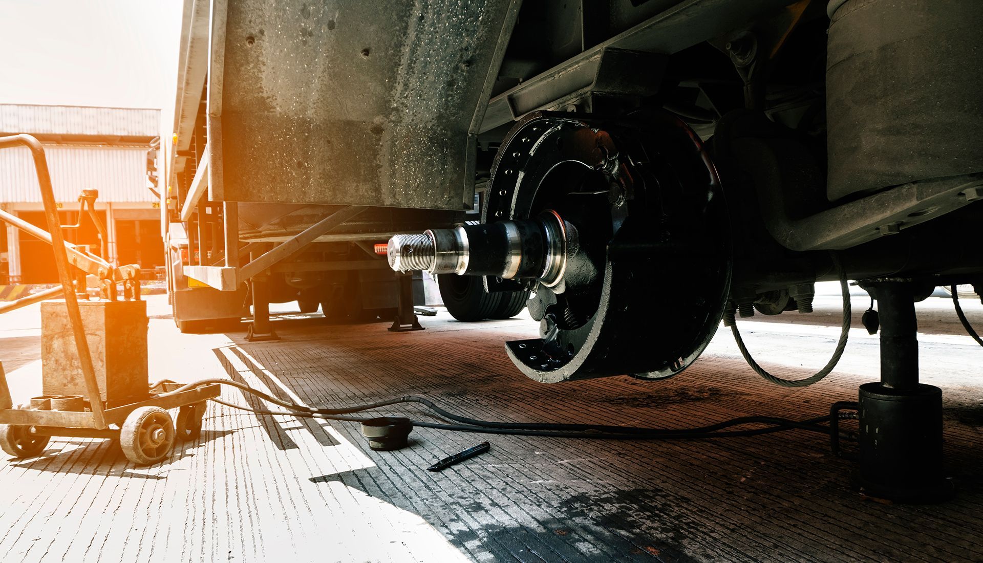 Undercarriage of a vehicle undergoing repair: wheel removed, tools and support jacks visible on a concrete surface.