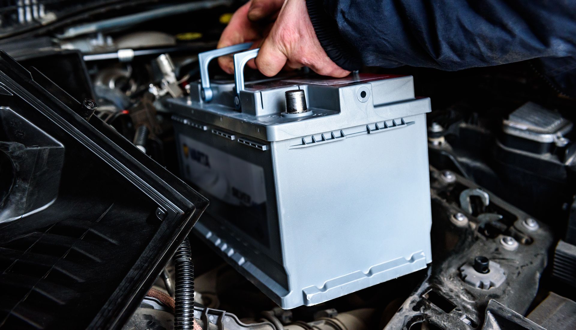 Hand lifting a car battery from engine compartment.