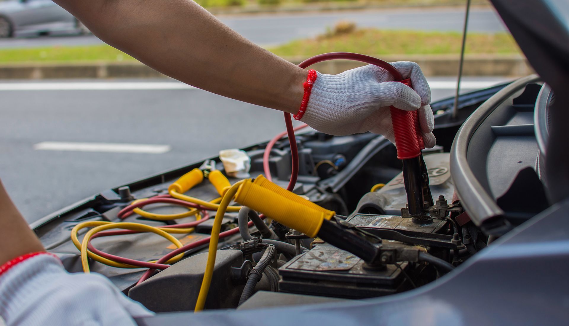 Person using jumper cables to jump-start a car battery in an engine bay.