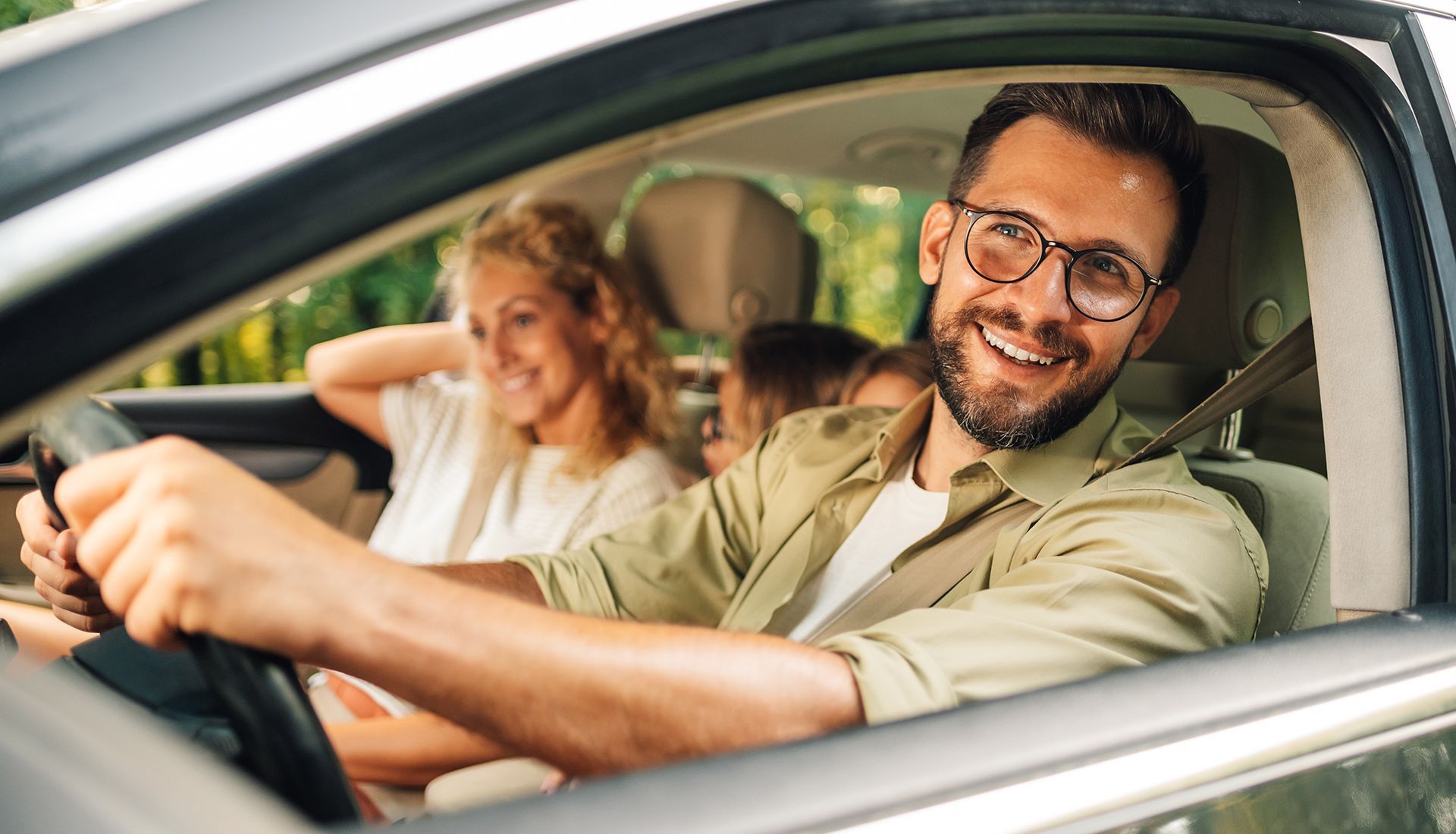 Man in car, smiling, driving with passengers.