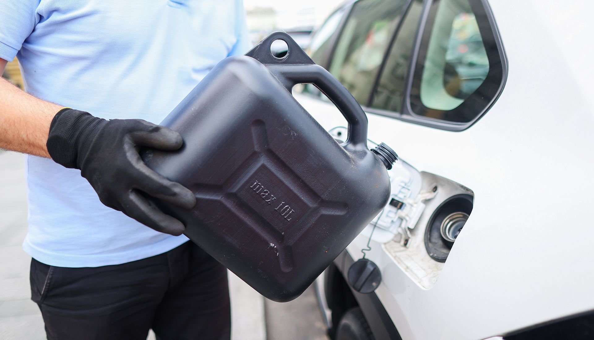 Person in black gloves pouring gasoline from a black container into a white car.