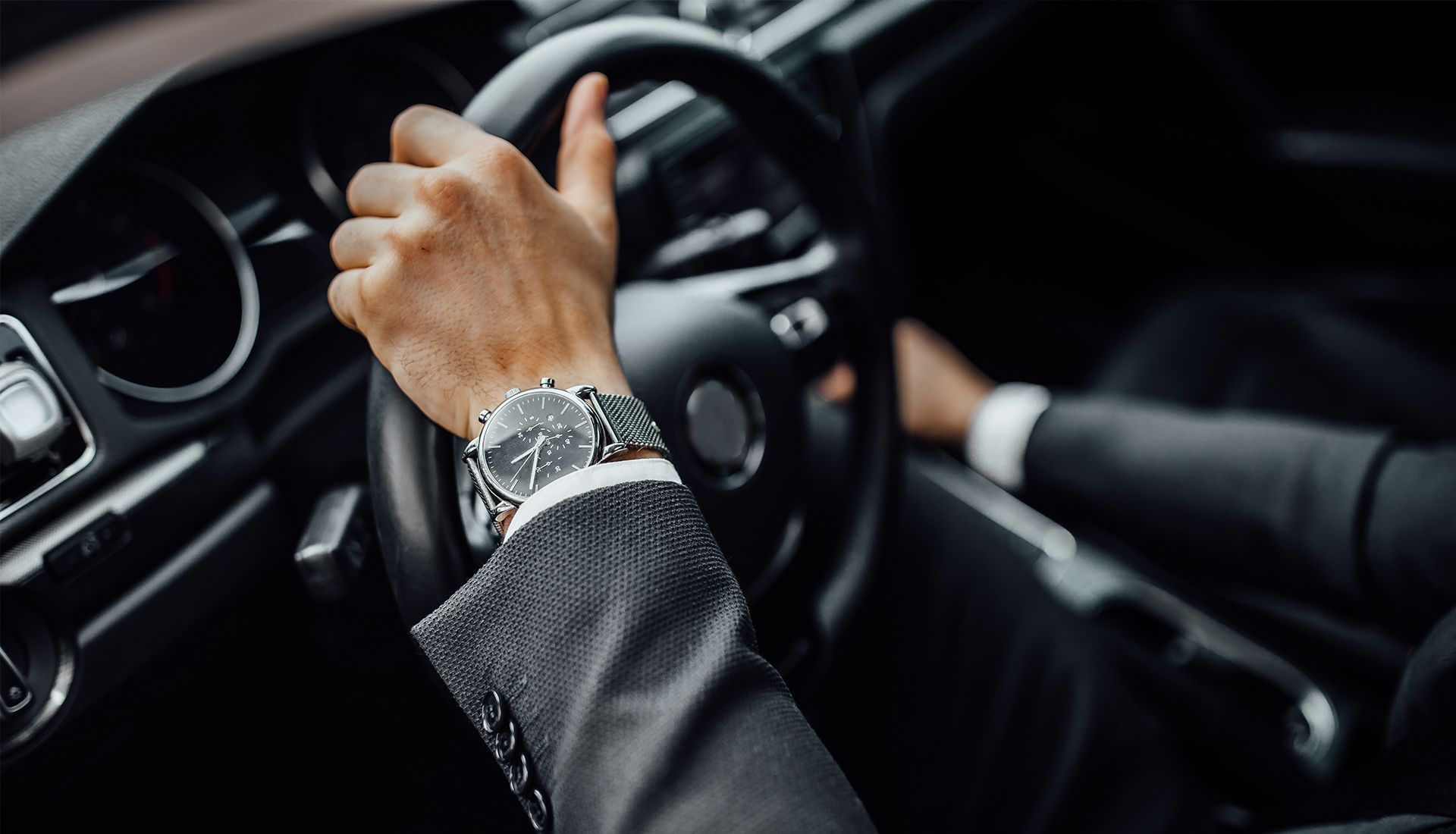 Person wearing a suit driving a car, hands on the steering wheel, and wearing a watch.