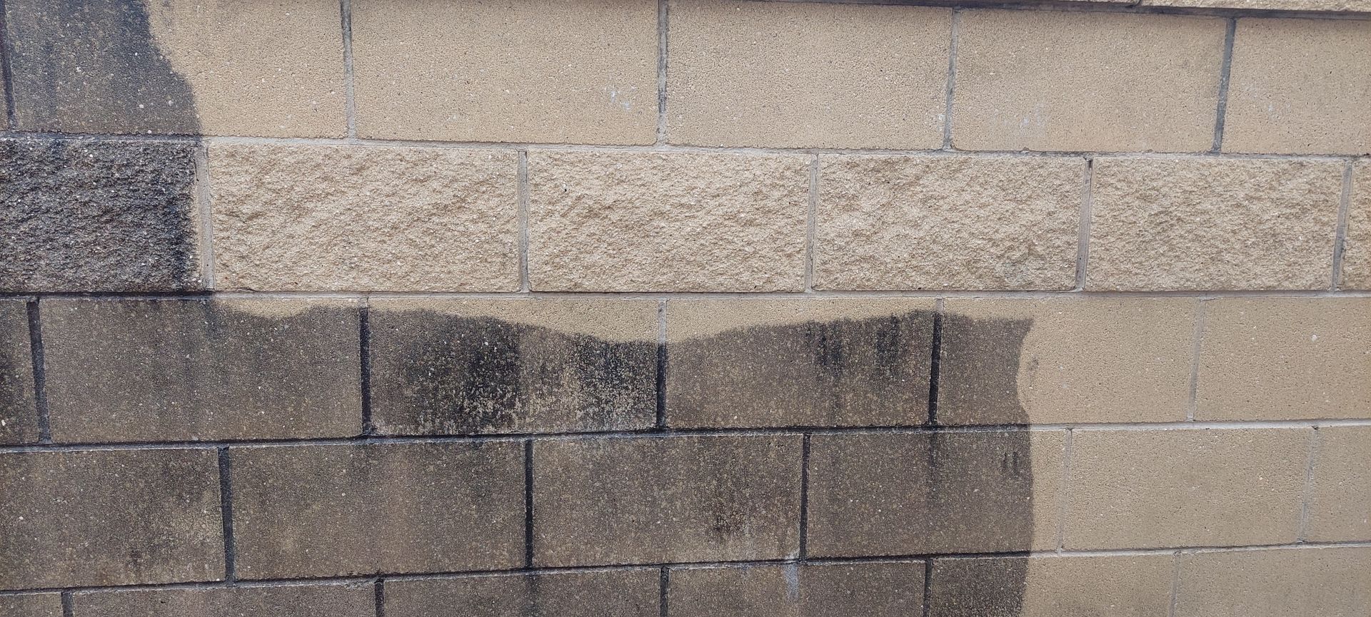 A beige concrete block wall featuring a distinct, dark wet patch covering the lower left side.