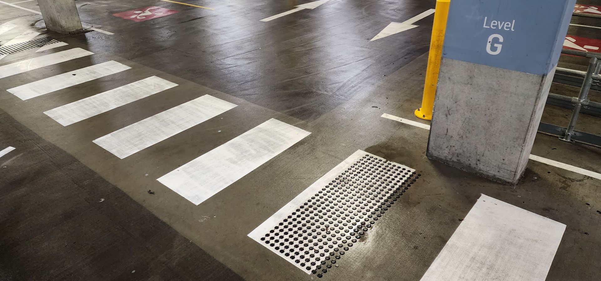 A pedestrian crosswalk in a parking garage with a tactile warning strip, next to a pillar marked Level G.