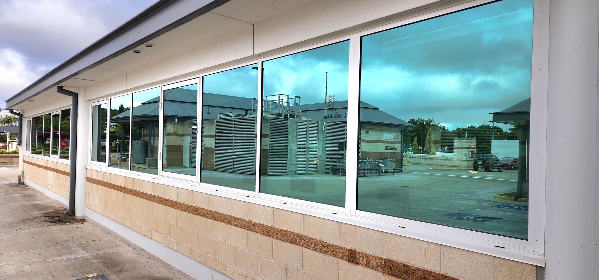A row of windows with blue-tinted reflective glass set into a tan brick building exterior under a cloudy sky.